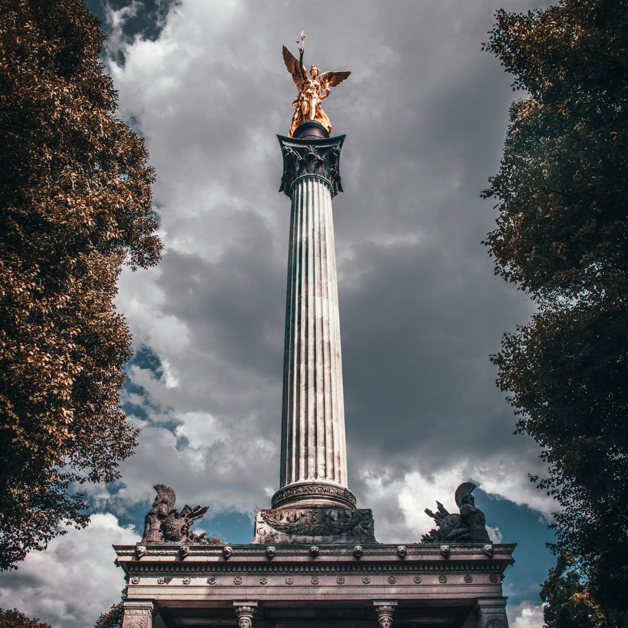 Friedensengel in München nahe Prinzregentenplatz – Blick auf die goldene Statue und Säule bei dramatischem Himmel.